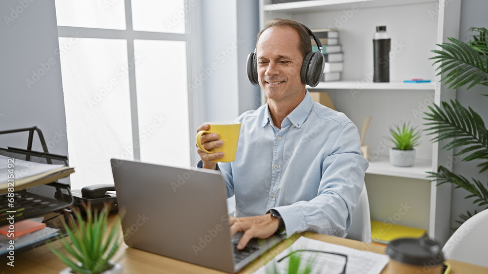 Cheerful middle age man, a successful executive, joyfully working at his office desk, listening to music and sipping his morning espresso coffee, brightening up the indoor workplace. Cheerful middle age man, a successful executive, joyfully working at his office desk, listening to music and sipping his morning espresso coffee, brightening up the indoor workplace.
