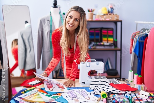 Young blonde woman tailor smiling confident looking clothing design at tailor shop photo