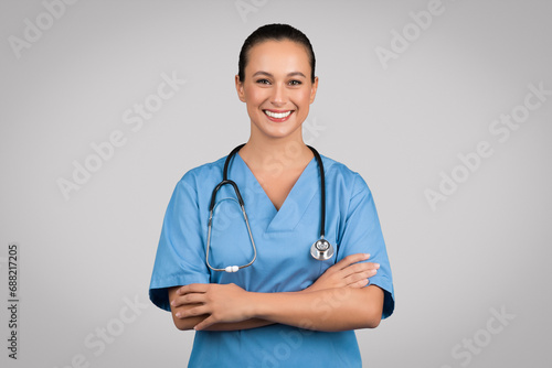 Portrait of positive european woman nurse posing with crossed arms and smiling at camera over grey studio background photo