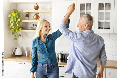 Portrait Of Cheerful Older Couple Dancing Together In Kitchen Interior