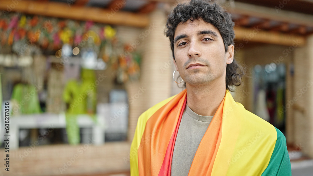 Young hispanic man wearing rainbow flag with relaxed expression at street Young hispanic man wearing rainbow flag with relaxed expression at street