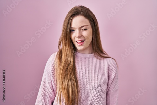 Young caucasian woman standing over pink background winking looking at the camera with sexy expression, cheerful and happy face.