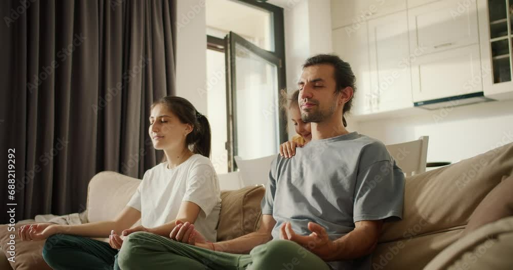 A brunette girl in a white T-shirt together with her husband, a brunette man in a gray T-shirt, meditates while sitting on light brown daughter girl, a little brunette girl in a yellow dress A brunette girl in a white T-shirt together with her husband, a brunette man in a gray T-shirt, meditates while sitting on light brown daughter girl, a little brunette girl in a yellow dress