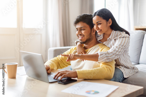 Happy young indian couple websurfing on laptop together at home photo