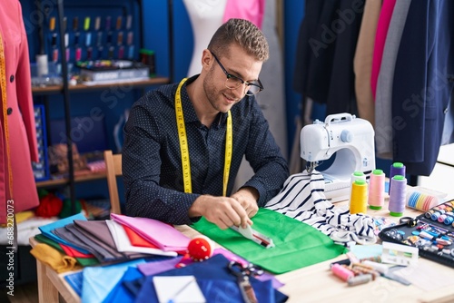 Young caucasian man tailor smiling confident make mark on cloth at clothing factory
