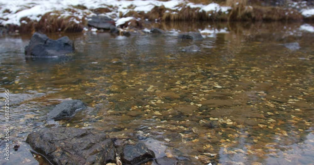 Rocks and pebbles lie beneath the flowing shallow water on a snowy day Rocks and pebbles lie beneath the flowing shallow water on a snowy day