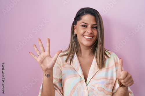 Blonde woman standing over pink background showing and pointing up with fingers number six while smiling confident and happy. © Krakenimages.com