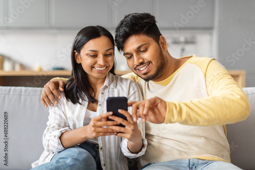 Smiling Young Indian Couple Using Smartphone And Embracing Together At Home