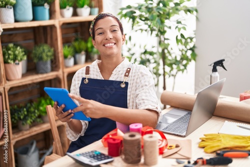 Young beautiful hispanic woman florist smiling confident using touchpad and laptop at florist