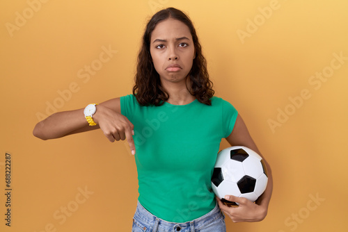 Young hispanic woman holding ball pointing down looking sad and upset, indicating direction with fingers, unhappy and depressed. © Krakenimages.com