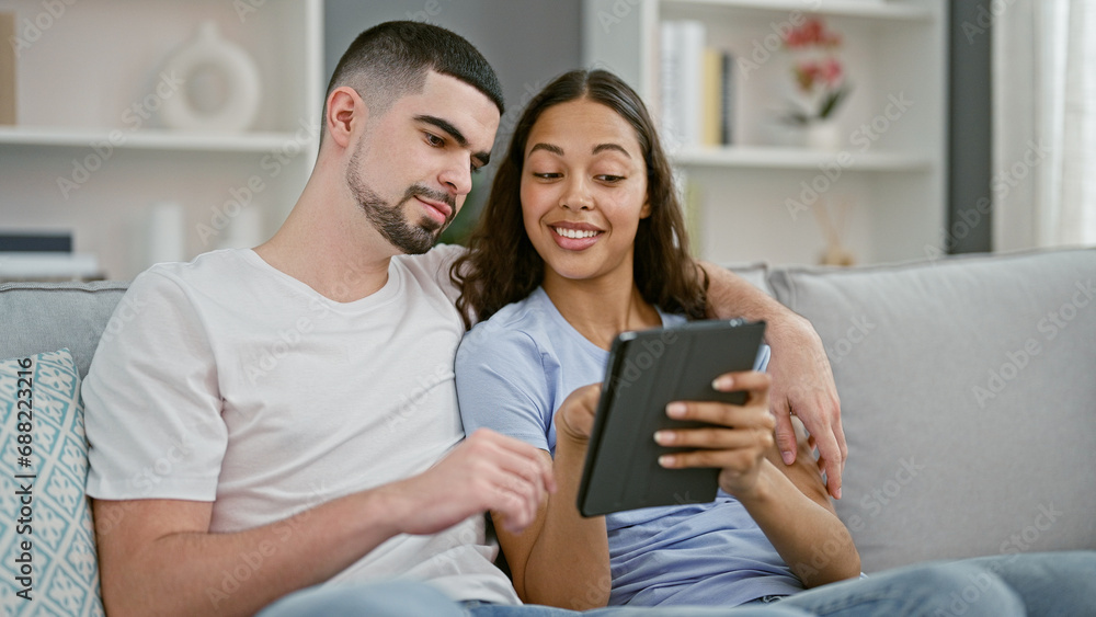 Smiling beautiful couple enjoying technology together at home, casual lifestyle of confident man and woman sitting on sofa, using touchpad