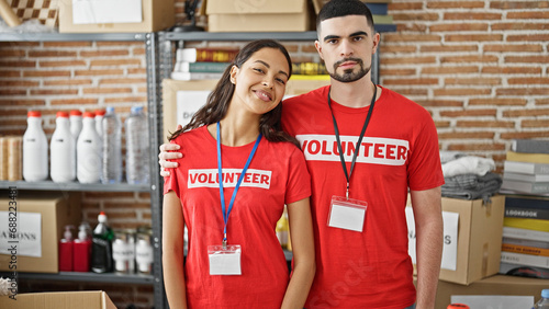 Smiling man and woman volunteers enjoy hugging each other, standing in charity center, unity in volunteer work
