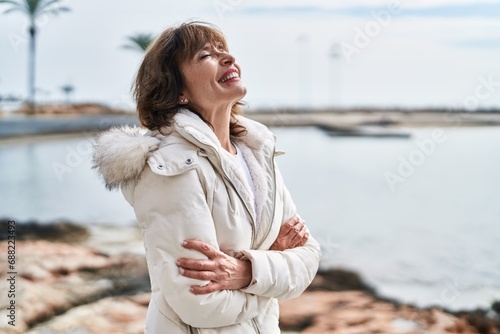 Middle age woman standing with arms crossed gesture breathing at seaside