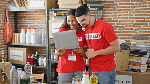 Man and woman volunteers smiling, working on laptop at charity center, standing together in service for community photo