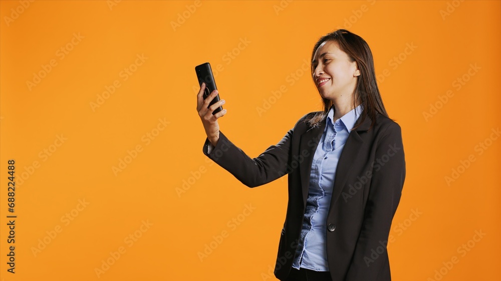 Filipino employee connecting online on videocall using smartphone, standing over orange background. Young woman with confidence answering videoconference connection on internet. Filipino employee connecting online on videocall using smartphone, standing over orange background. Young woman with confidence answering videoconference connection on internet.