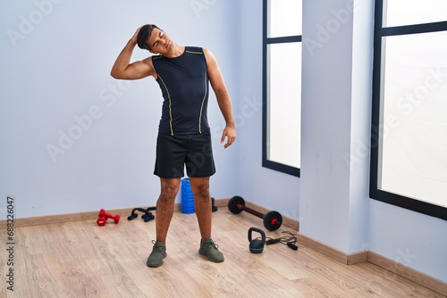 Young hispanic man stretching head standing at sport center