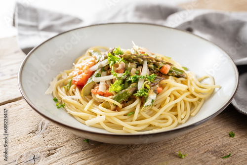 Spaghetti with vegetable sauce of green asparagus and tomatoes with parmesan and parsley garnish in a plate on a rustic wooden table  selected focus
