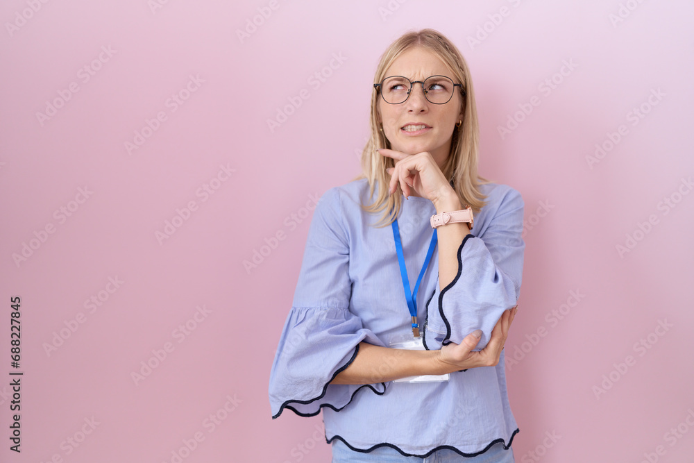 Young caucasian business woman wearing id card thinking worried about a question, concerned and nervous with hand on chin Young caucasian business woman wearing id card thinking worried about a question, concerned and nervous with hand on chin