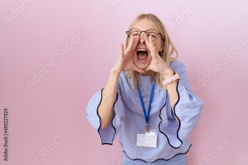 Young caucasian business woman wearing id card shouting angry out loud with hands over mouth