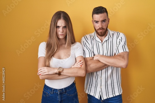 Young couple standing over yellow background skeptic and nervous, disapproving expression on face with crossed arms. negative person.