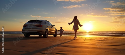 Seen from behind next to the car is the mother and daughter running happily along the beach at sunset photo