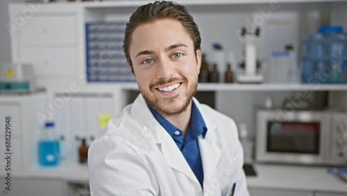 Young hispanic man scientist smiling confident sitting on chair at laboratory