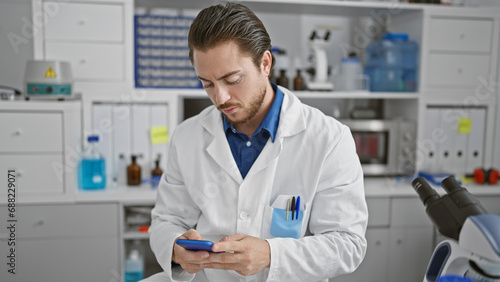 Young hispanic man scientist using smartphone at laboratory