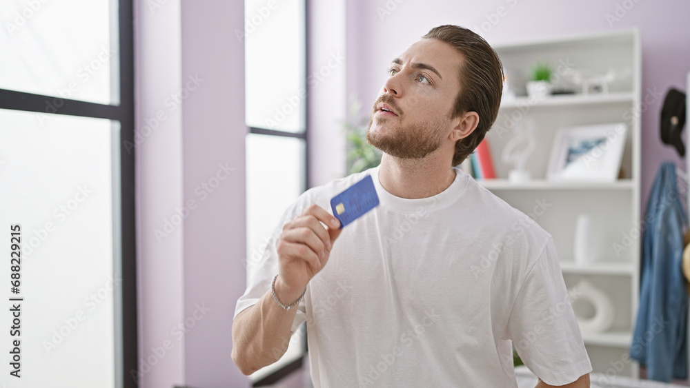 Young hispanic man holding credit card thinking at home Young hispanic man holding credit card thinking at home