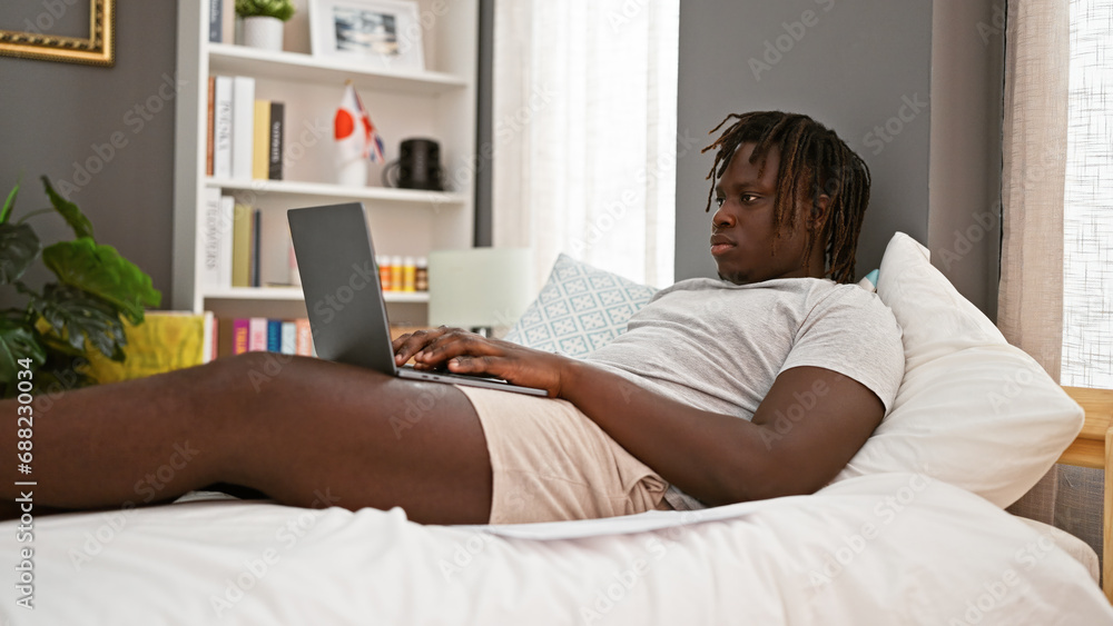African american man using laptop lying on bed at bedroom African american man using laptop lying on bed at bedroom