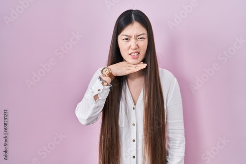 Photography Chinese young woman standing over pink background cutting throat with hand as kn