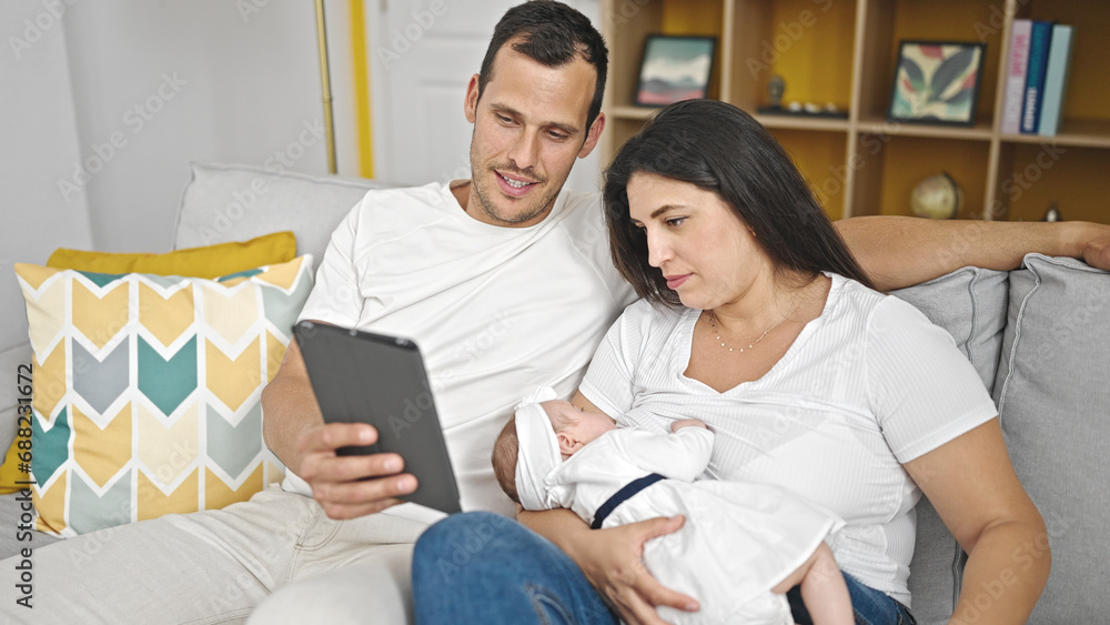 Family of three using touchpad sitting on the sofa at home Family of three using touchpad sitting on the sofa at home