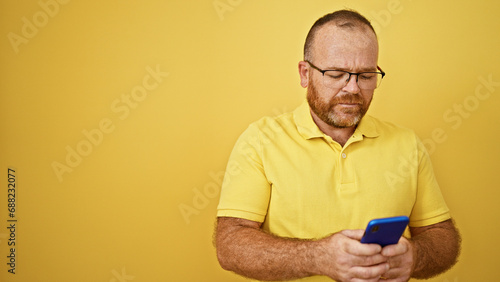 Caucasian man using smartphone with serious expression over isolated yellow background