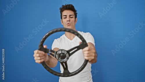 Young hispanic man smiling confident using steering wheel as a driver over isolated blue background