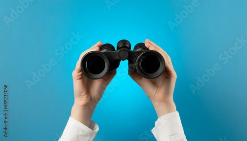 Female hands hold black binoculars on a bright yellow background