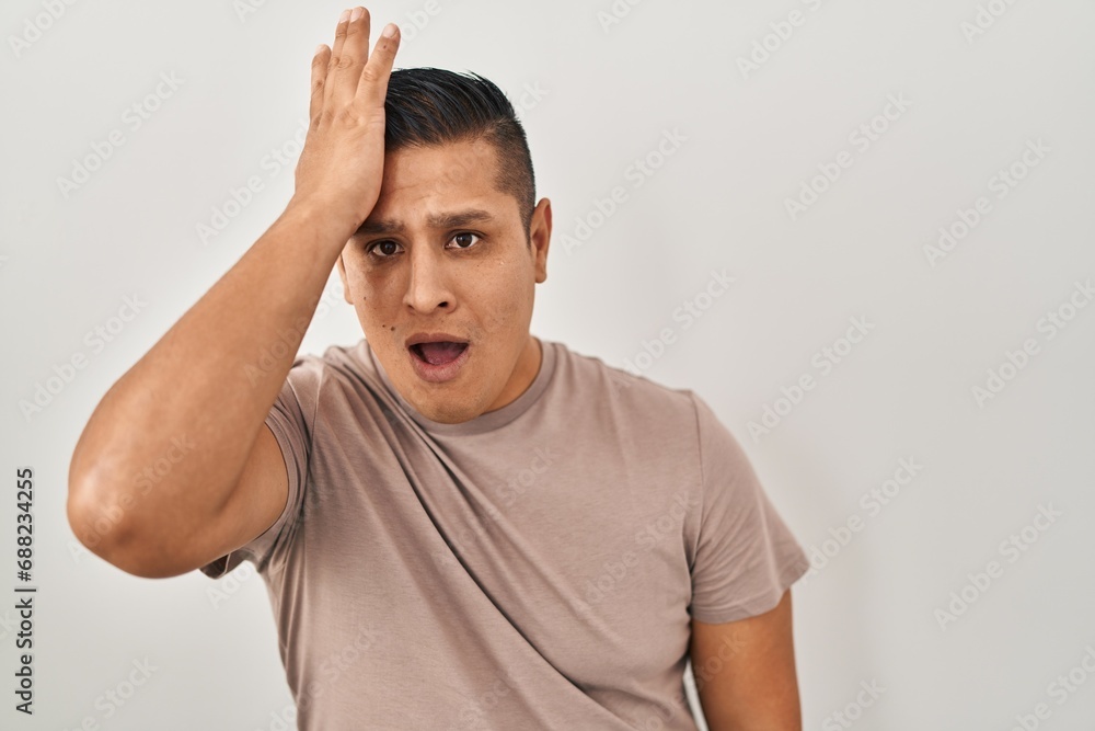 Hispanic young man standing over white background surprised with hand on head for mistake, remember error. forgot, bad memory concept. Hispanic young man standing over white background surprised with hand on head for mistake, remember error. forgot, bad memory concept.