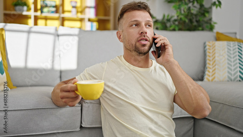 Young man talking on smartphone drinking coffee at home