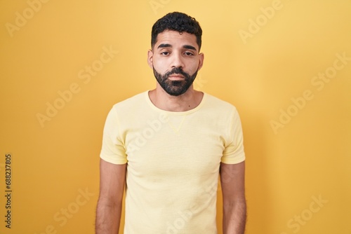 Hispanic man with beard standing over yellow background looking sleepy and tired, exhausted for fatigue and hangover, lazy eyes in the morning.