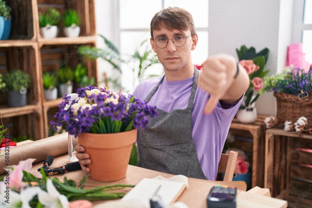 Caucasian blond man working at florist shop looking unhappy and angry showing rejection and negative with thumbs down gesture. bad expression.