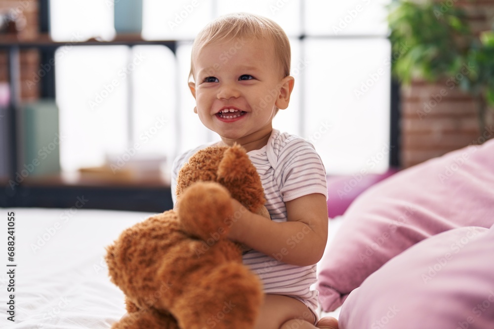 Adorable toddler playing with teddy bear sitting on bed at bedroom Adorable toddler playing with teddy bear sitting on bed at bedroom