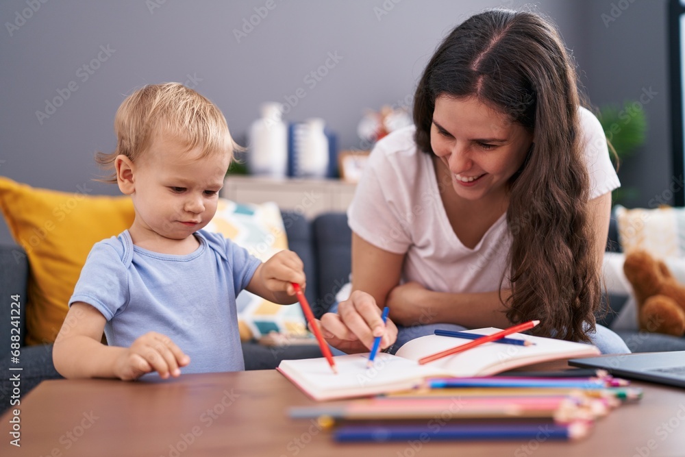 Mother and son sitting on sofa drawing on notebook at home