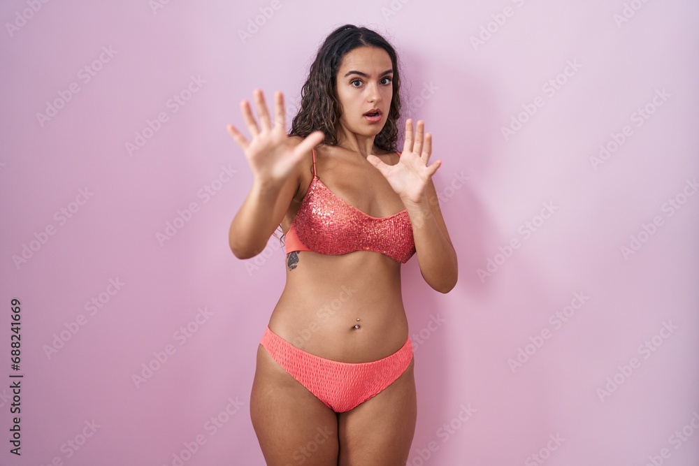 Obraz premium Young hispanic woman wearing lingerie over pink background afraid and terrified with fear expression stop gesture with hands, shouting in shock. panic concept.