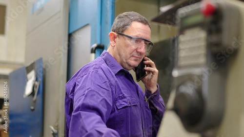 Video of a mature engineer using phone while working in a cnc factory using control machine