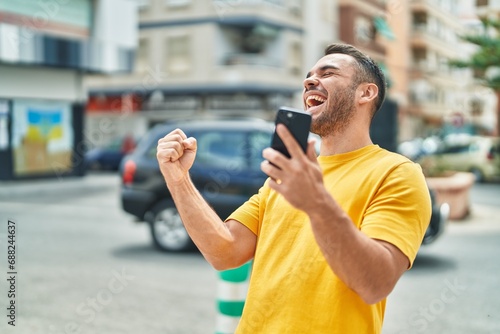 Young hispanic man using smartphone with winner expression at street