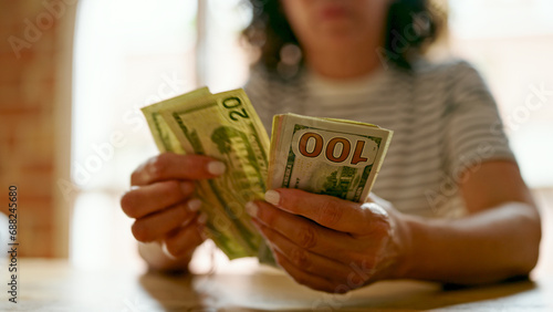 Middle age hispanic woman counting dollars at home