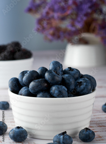 Fresh blueberries in a white ceramic bowl on rustic style white wooden background.