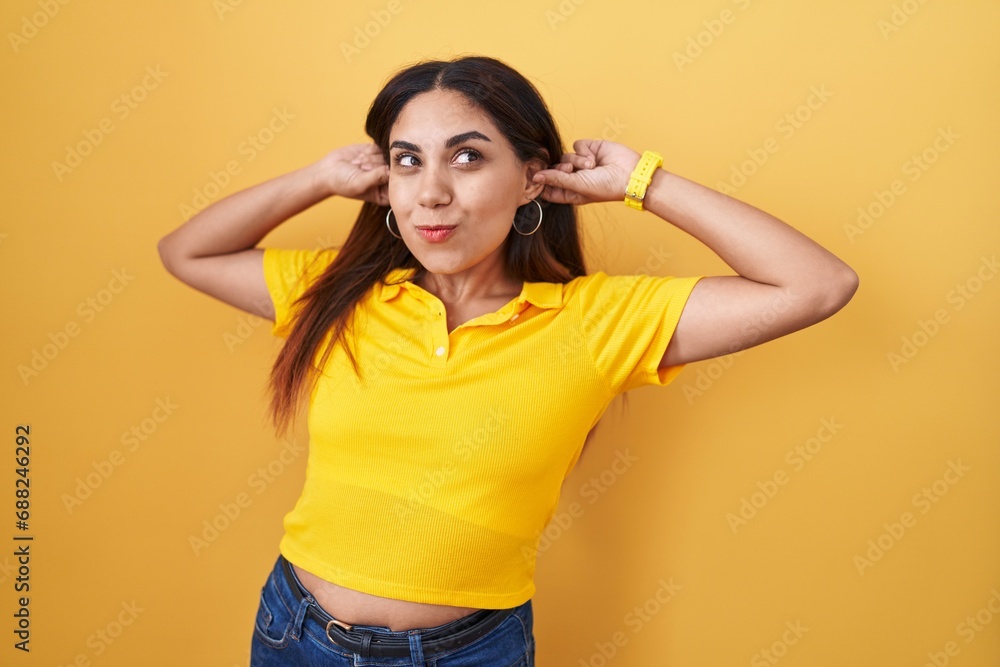 Young arab woman standing over yellow background smiling pulling ears with fingers, funny gesture. audition problem Young arab woman standing over yellow background smiling pulling ears with fingers, funny gesture. audition problem