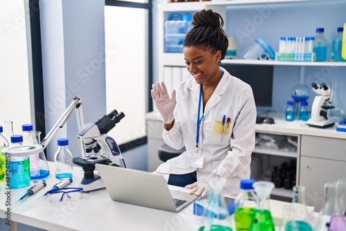 Young african american with braids working at scientist laboratory with laptop looking positive and happy standing and smiling with a confident smile showing teeth