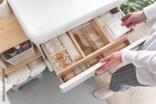 Top view of woman hands neatly organizing bathroom amenities and toiletries in drawer in bathroom.