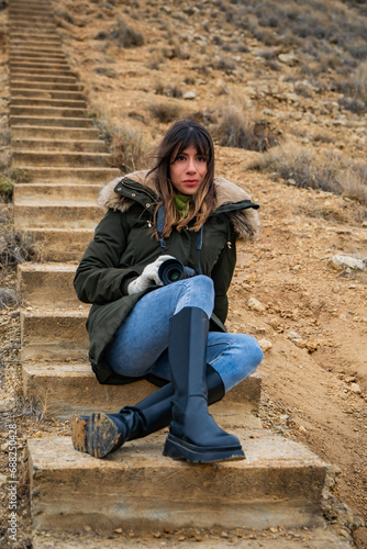 Brunette in jeans, black boots. Sitting on desert stairs, Spain's Bardenas Reales.
