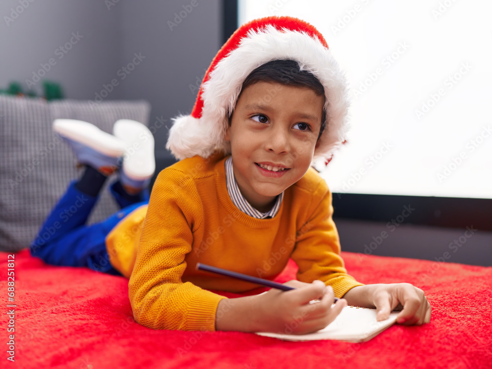 Adorable hispanic boy wearing christmas hat writing santa claus letter at home Adorable hispanic boy wearing christmas hat writing santa claus letter at home